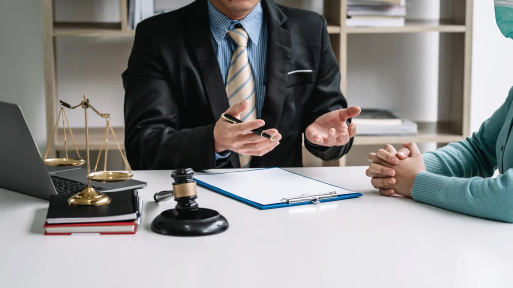 A lawyer in a suit gestures during a discussion with a client, with a scale, gavel, and open laptop on the table, emphasizing the legal aspects of a DUI conviction and its impact on a professional license.