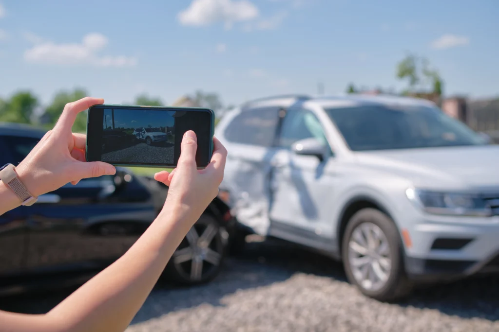 Person taking photo of dented white SUV after accident on sunny day