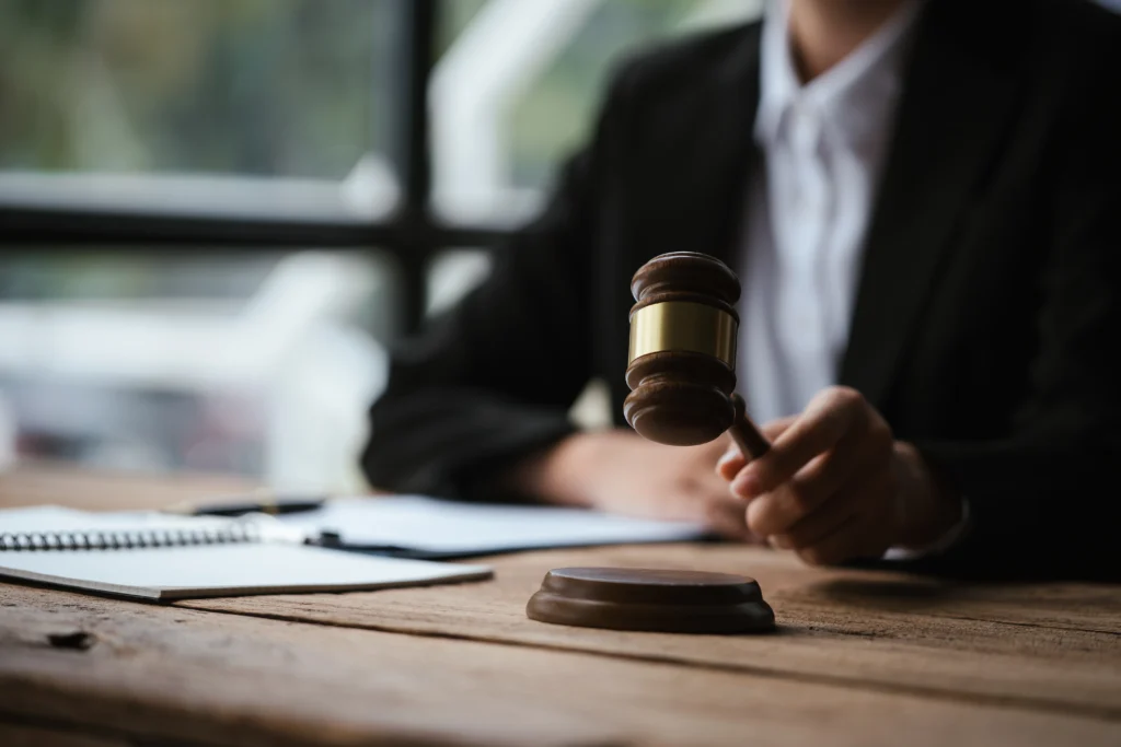 A lawyer in a suit holds a gavel over a table with legal papers, symbolizing a courtroom setting.