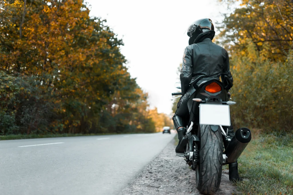 Motorcyclist in black gear on rural autumn road highlighting motorcycle safety.
