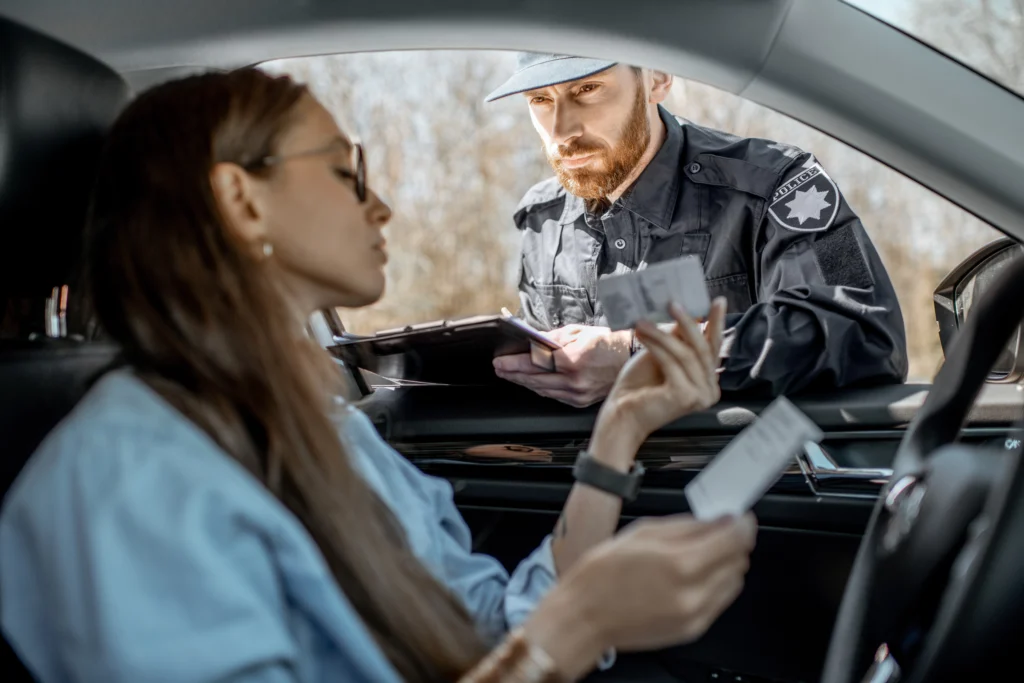 Police officer reviewing documents from woman in car, calm driver wearing sunglasses, official scene