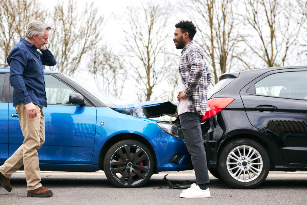 Two cars damaged from a rear-end collision on a road, with two men standing beside them looking concerned and discussing the accident — illustrating the aftermath of a wreck and the decision point for filing a car-accident claim.